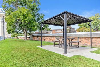 A picnic pavilion with a black roof is situated in a grassy area.